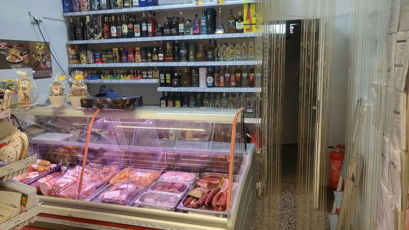 A counter with fresh meat and smoked meats, and a shelf with alcohol